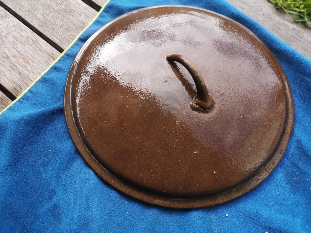 A rusty camp oven lid wet with a vinegar wash sits on a blue towel in our bid to rescue a rusted cast iron 